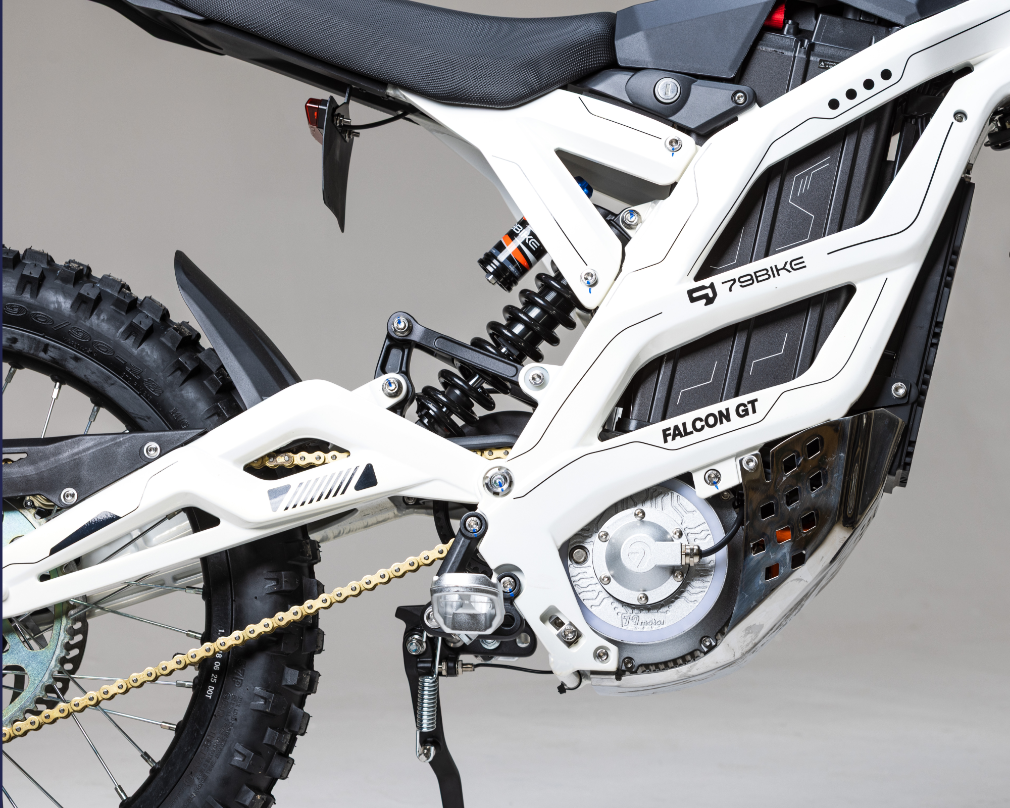 Close-up of white 79BIKE Falcon GT electric dirt bike rear section with suspension and chain.