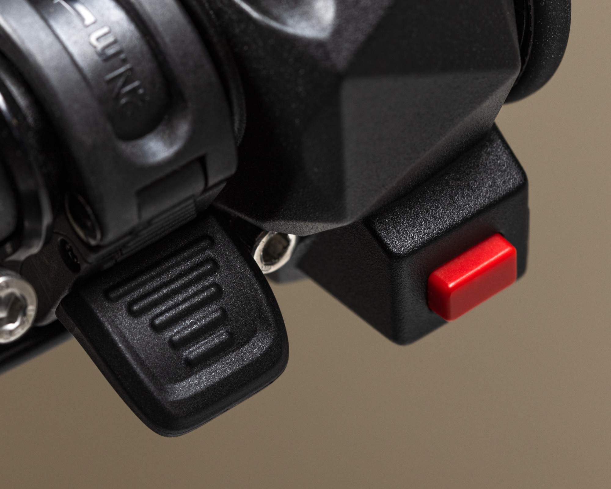 Close-up of a black motorcycle handlebar control with a red rectangular button and a textured black lever.