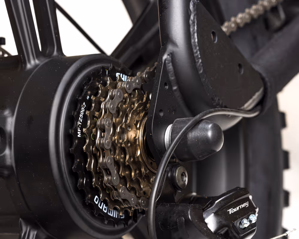 Close-up of a black bicycle's gear and chain mechanism with Shimano and Tourney parts visible.