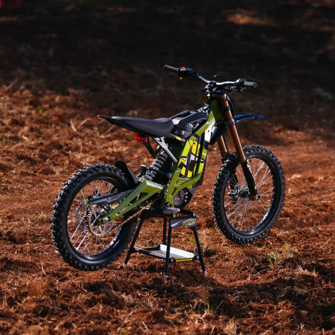 Electric dirt bike with knobby tires standing on a stand on dirt terrain.
