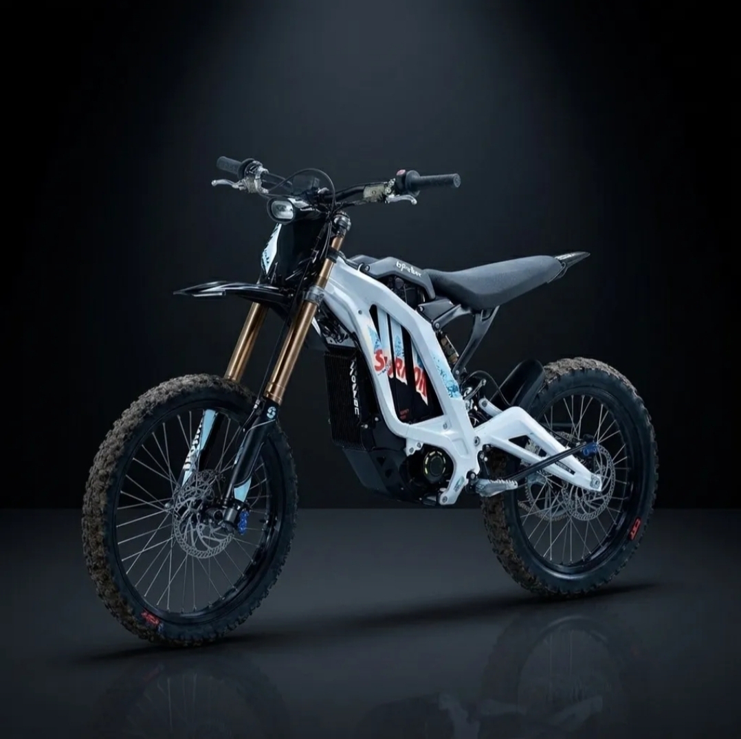 White and black electric dirt bike with knobby tires, front suspension forks, and a slim seat displayed on a reflective dark surface with a black background.