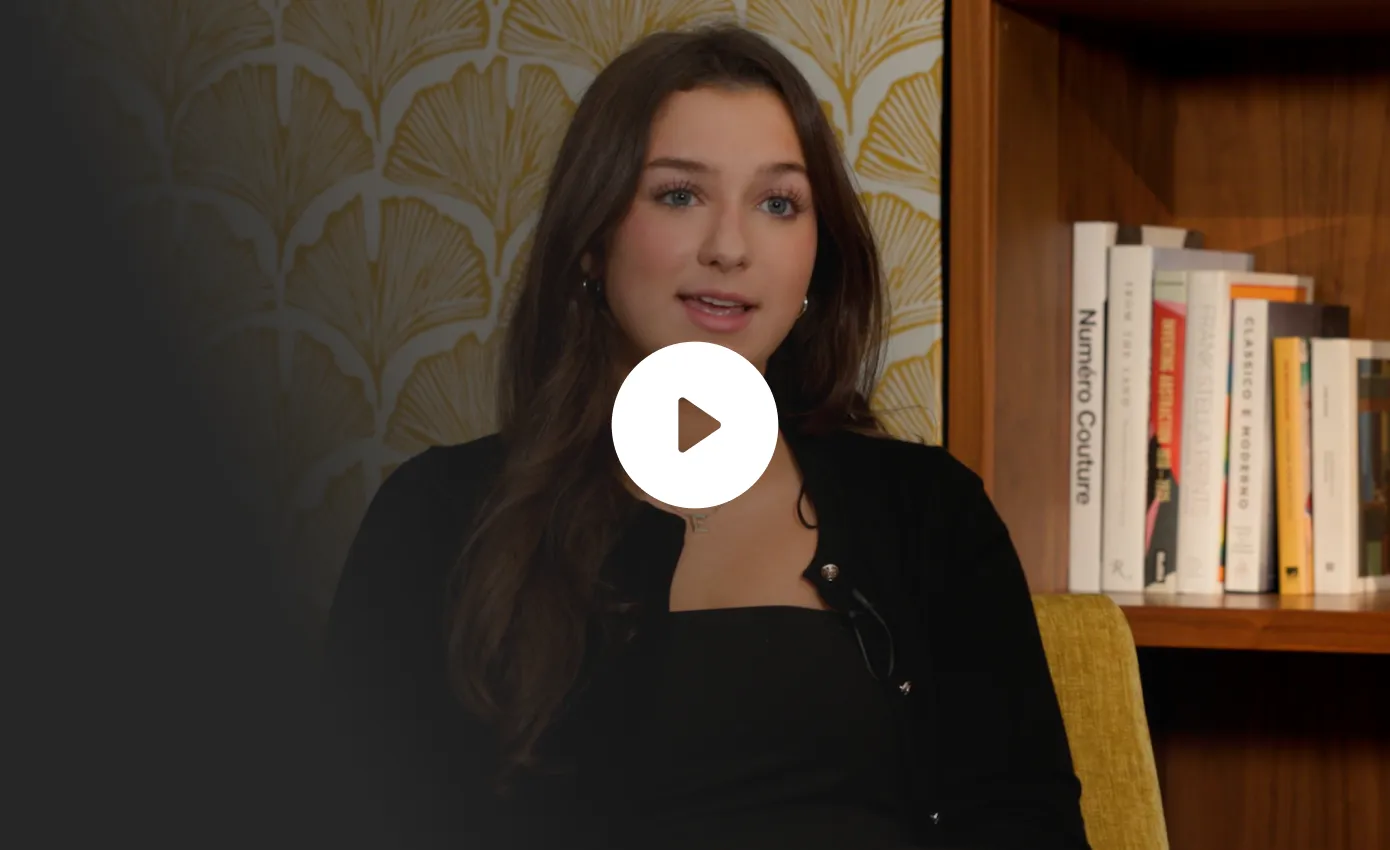 Young woman with long dark hair speaking in front of a bookshelf with various books.