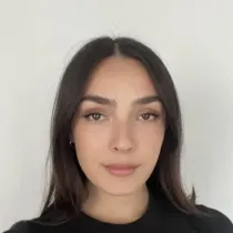 Portrait of a young woman with long dark hair wearing a black top against a plain light background.