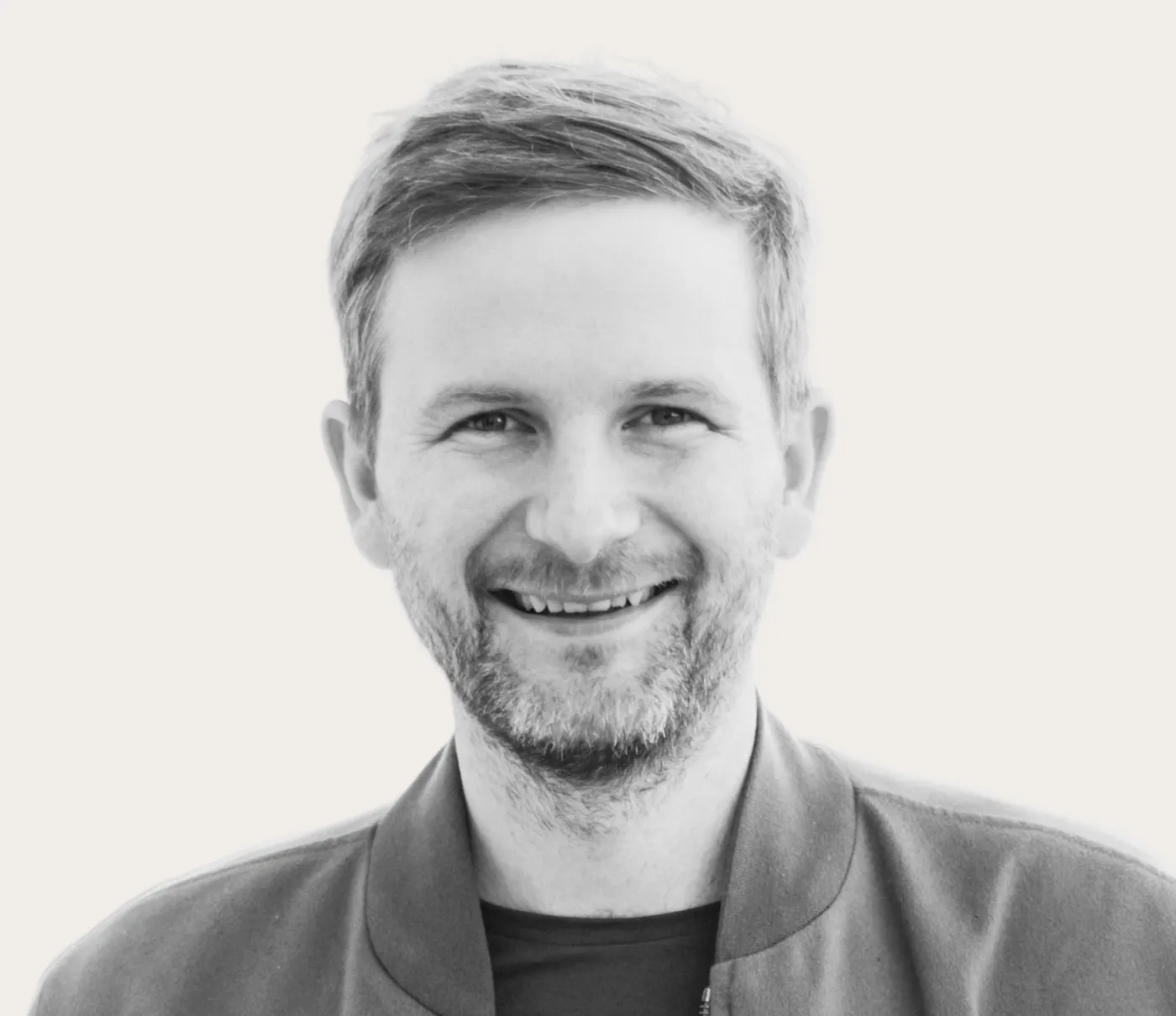 Black and white portrait of a smiling man with short hair and a beard wearing a jacket.