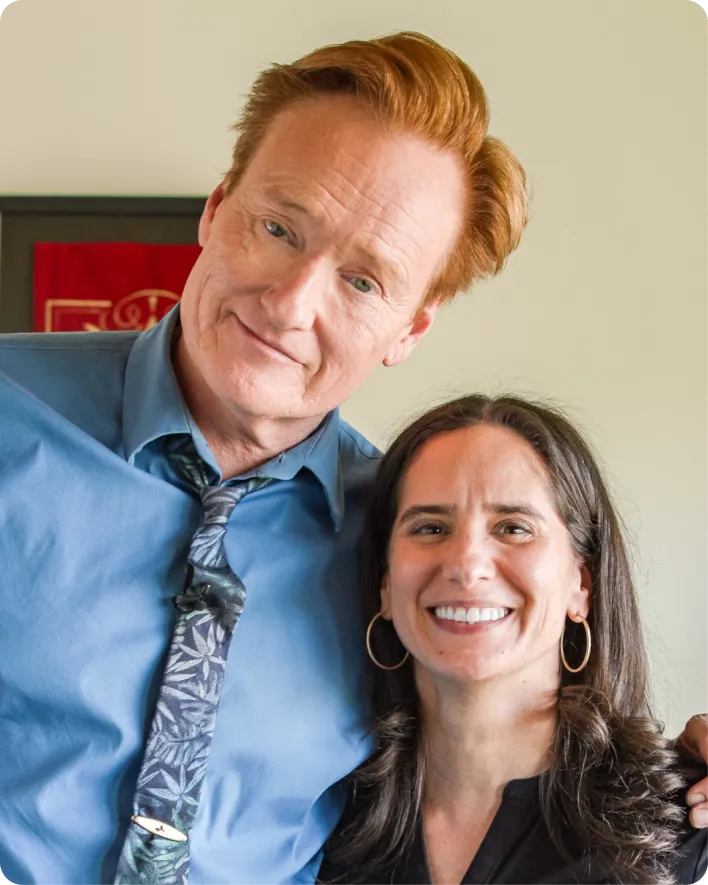 Man in blue shirt and patterned tie with arm around smiling woman with long dark hair and hoop earrings.