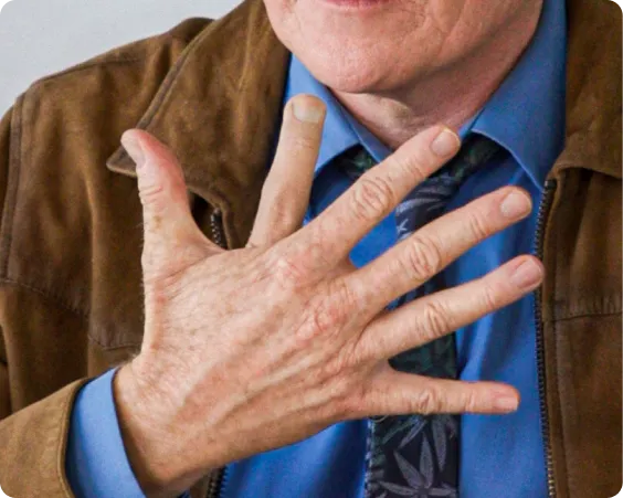 Close-up of a man's hand showing five fingers in front of his blue shirt and brown jacket.