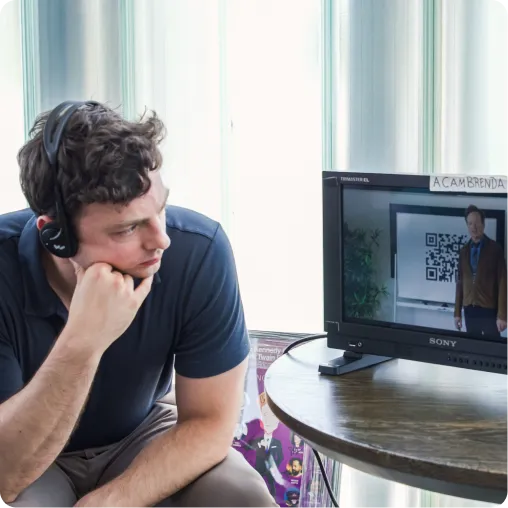 Man with headset watching a man presenting a QR code on a monitor at a round table.