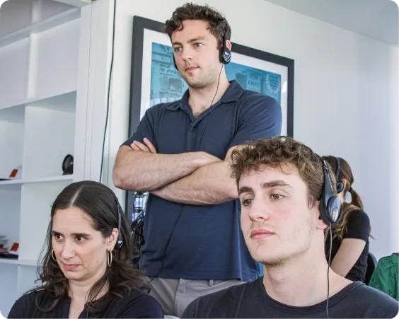 Three people wearing headsets focused on a task in a bright office with shelves and framed pictures.