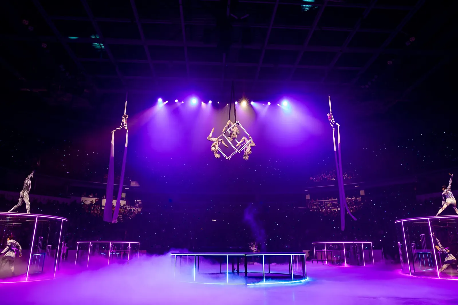 Aerialists and acrobats performing under purple light in the arena at TennoCon 2026