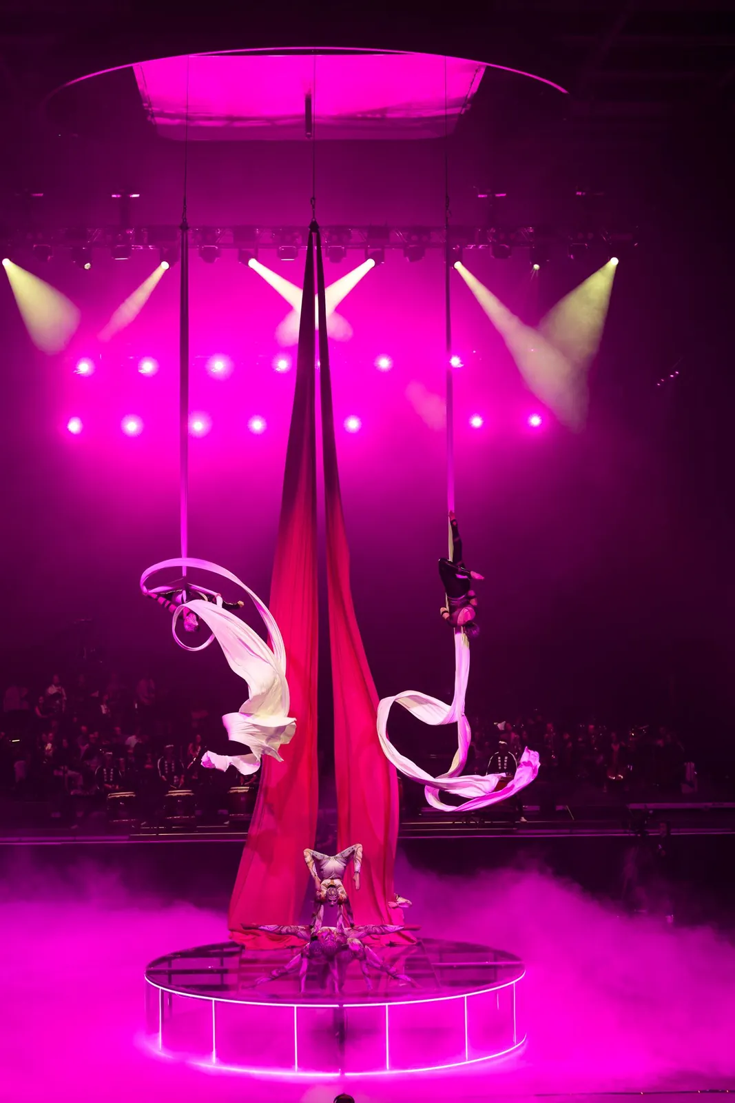 Aerialists on red silks above a stage in pink haze