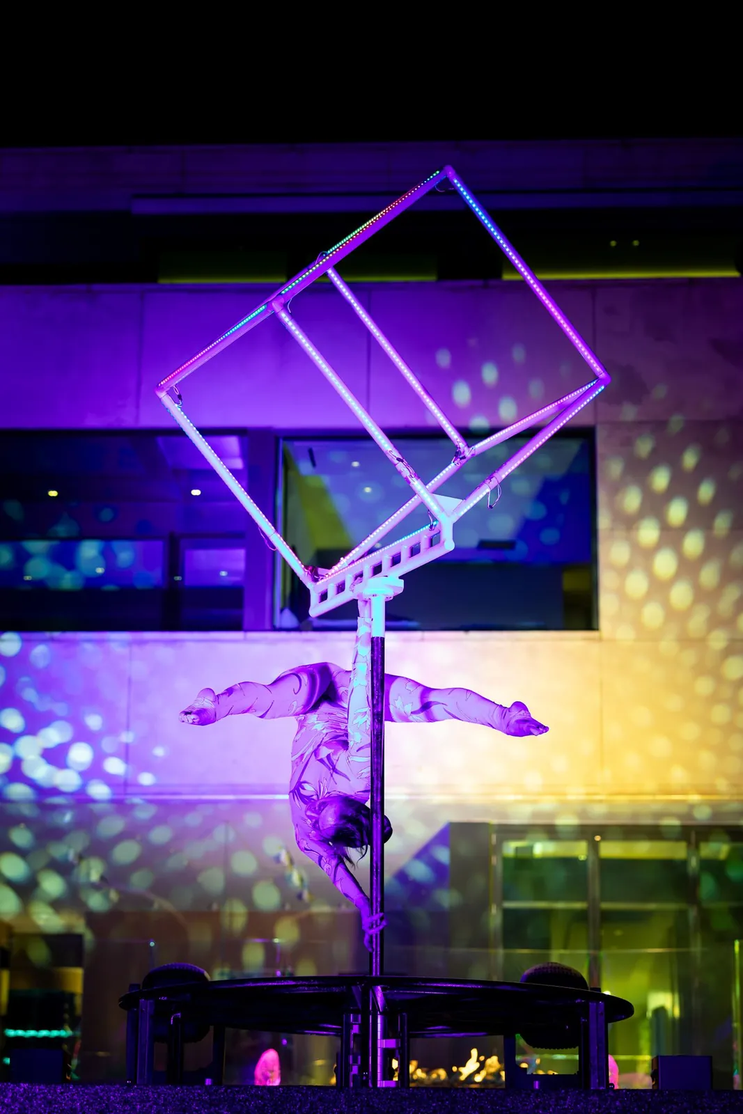 Aerialist balancing inside the LED cube under coloured light