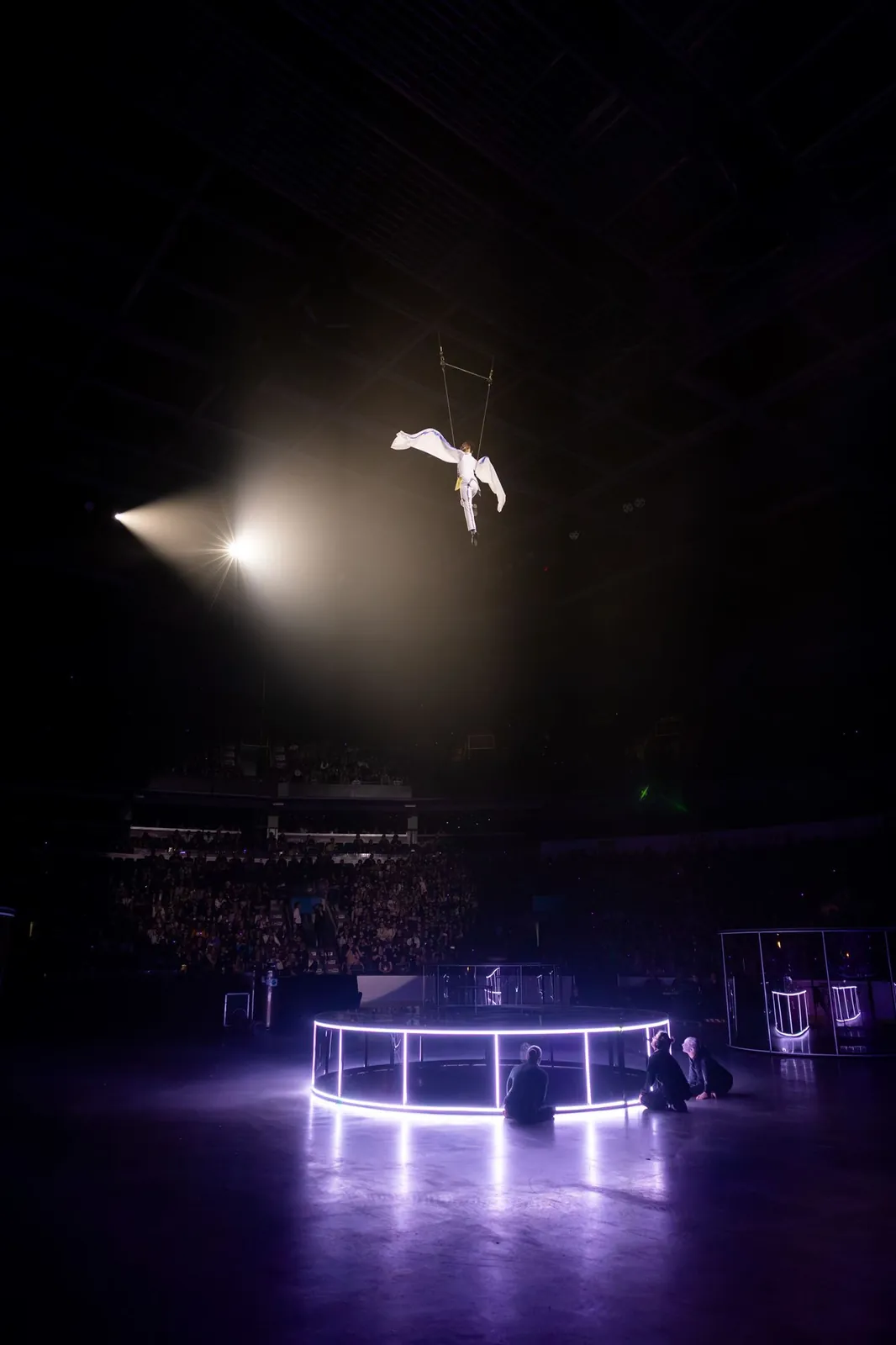 Aerialist in a harness suspended in a spotlight above an illuminated stage