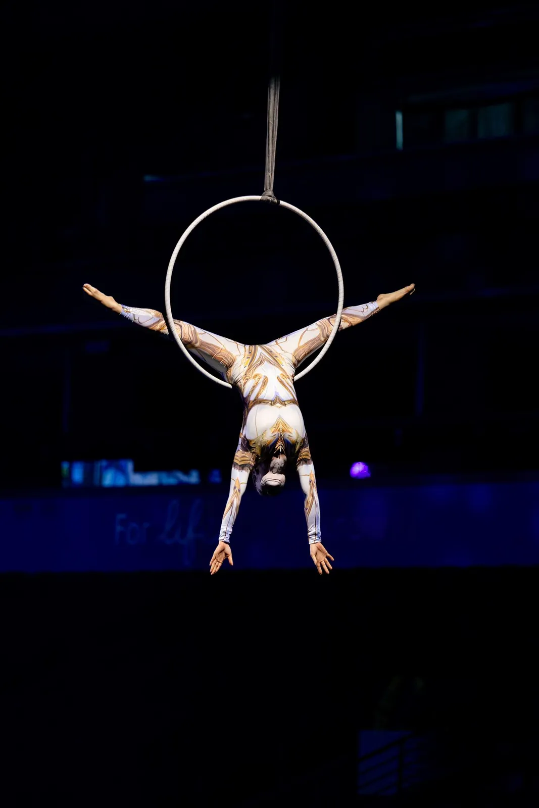 Aerial hoop performer in a split pose against a dark background
