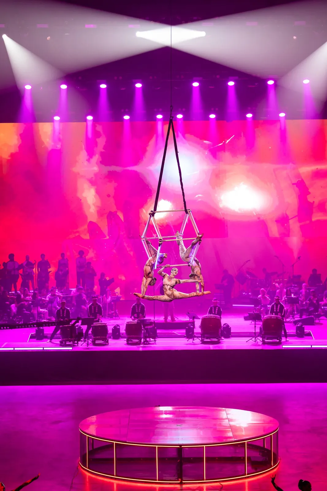 Aerial cube duo performing above an orchestra stage in pink lighting