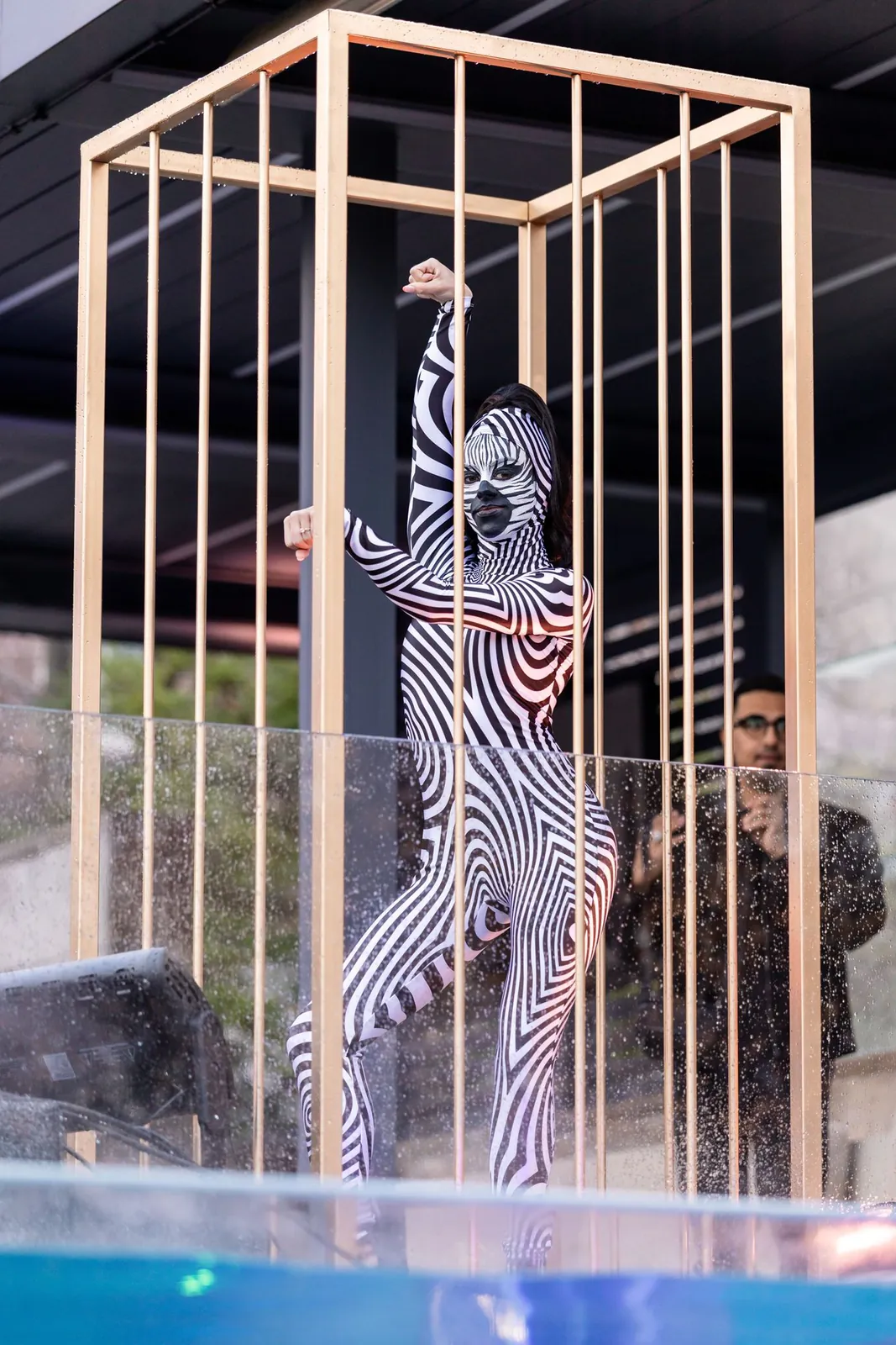 Model in a zebra-print bodysuit posing inside a gold cage