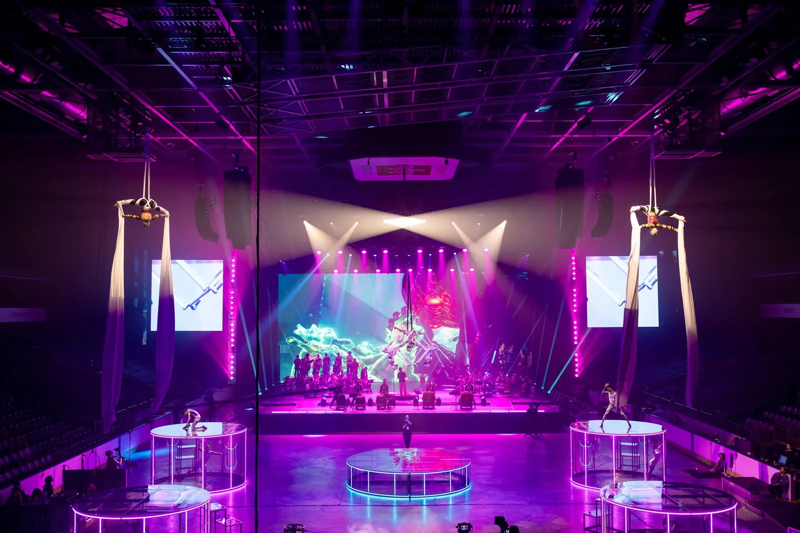 Synchronized aerialists performing above a stage in magenta light