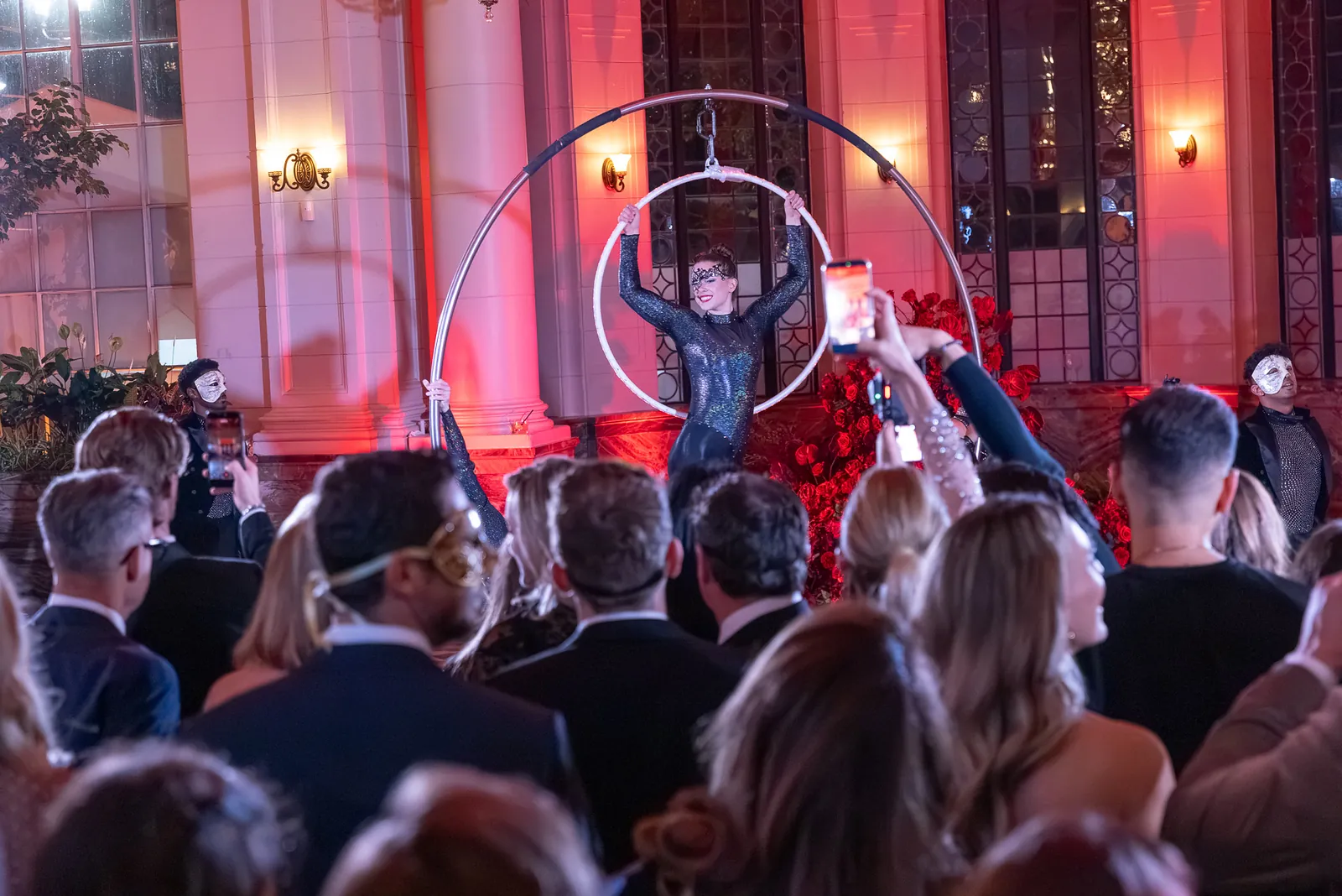 Aerial hoop performer above masquerade gala guests in a grand hall