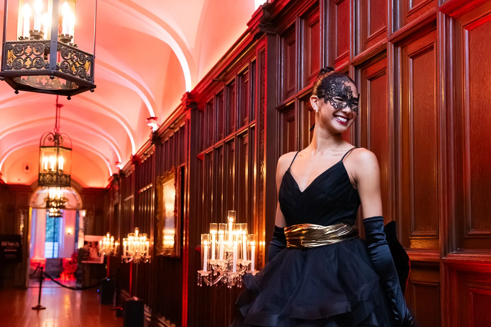 Masquerade performer in a black gown in a wood-panelled ballroom
