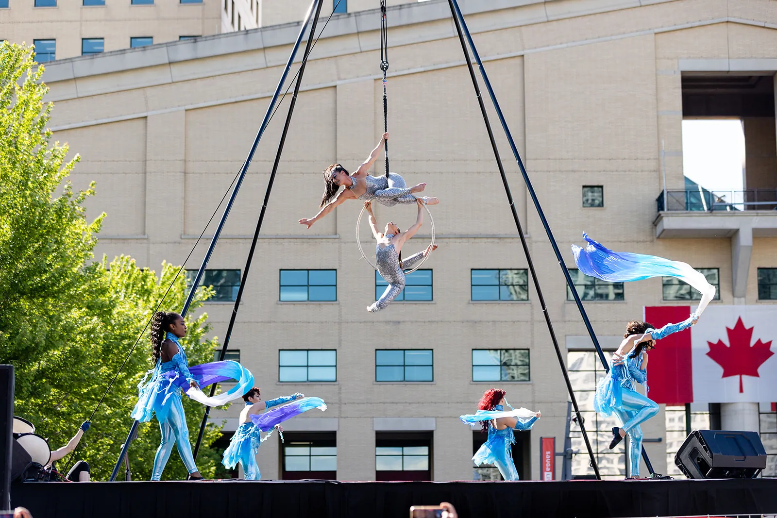 Aerial rig performers above an outdoor stage with dancers below