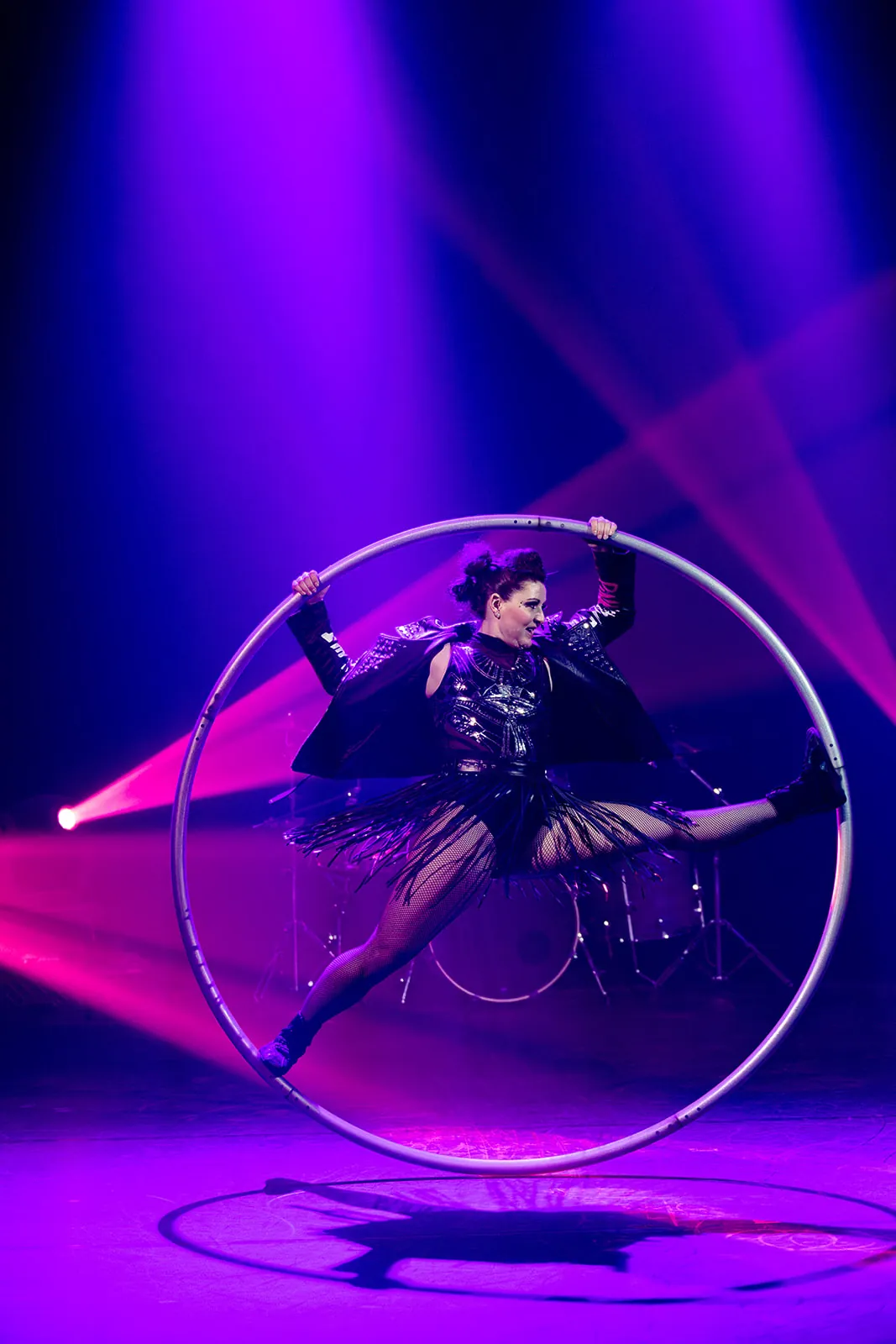 Cyr wheel artist in a split inside the wheel under pink lights
