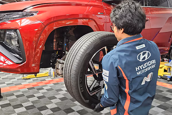 Technician in Hyundai Motorsport jacket installing a tyre on a red Hyundai SUV lifted in a garage.