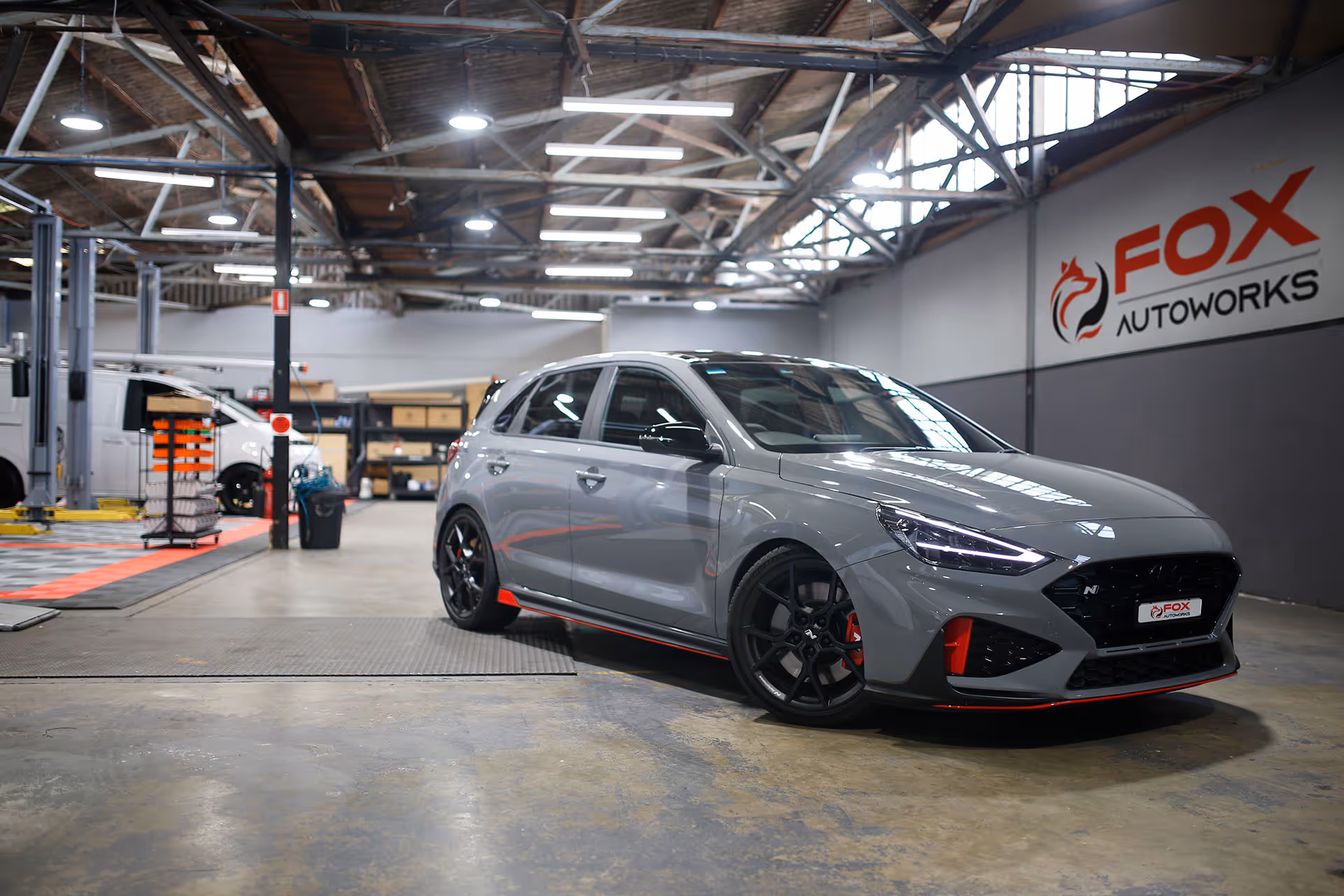 Gray sporty Hyundai i30N hatchback car with black rims parked inside a bright auto workshop.