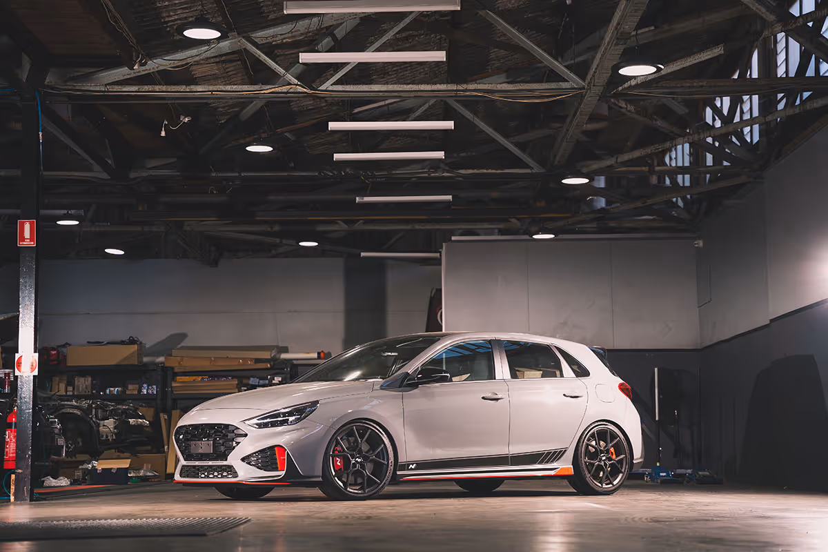 Gray sporty Hyundai i30N hatchback car with black wheels inside a dimly lit workshop