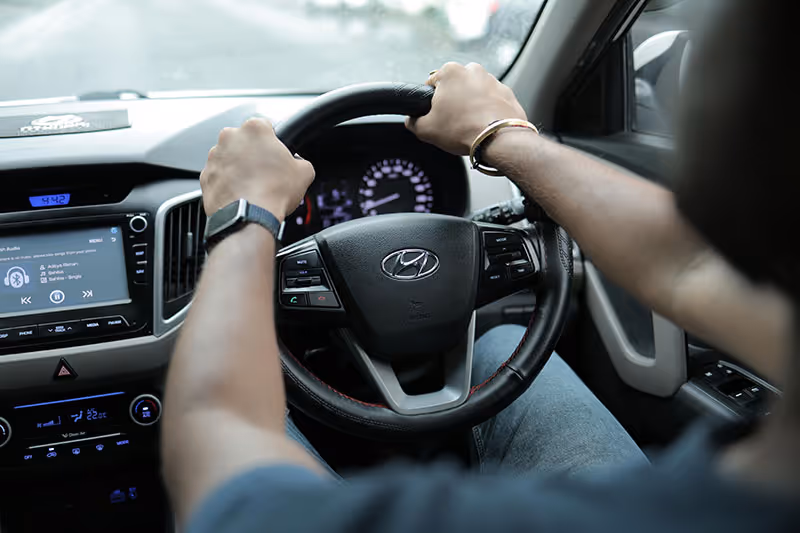 Mechanic taking a Hyundai for a road test drive, gripping steering wheel showing dashboard and infotainment screen.
