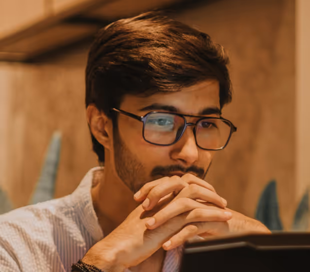 Man with glasses resting his chin on clasped hands, concentrating on a screen.