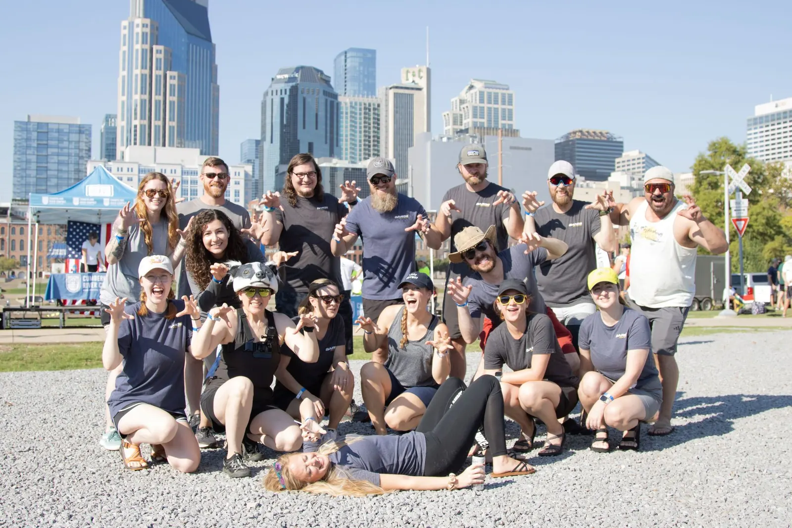 A group of Barge employees posing playfully with clawed hands in front of the Nashville skyline during an outdoor community event.