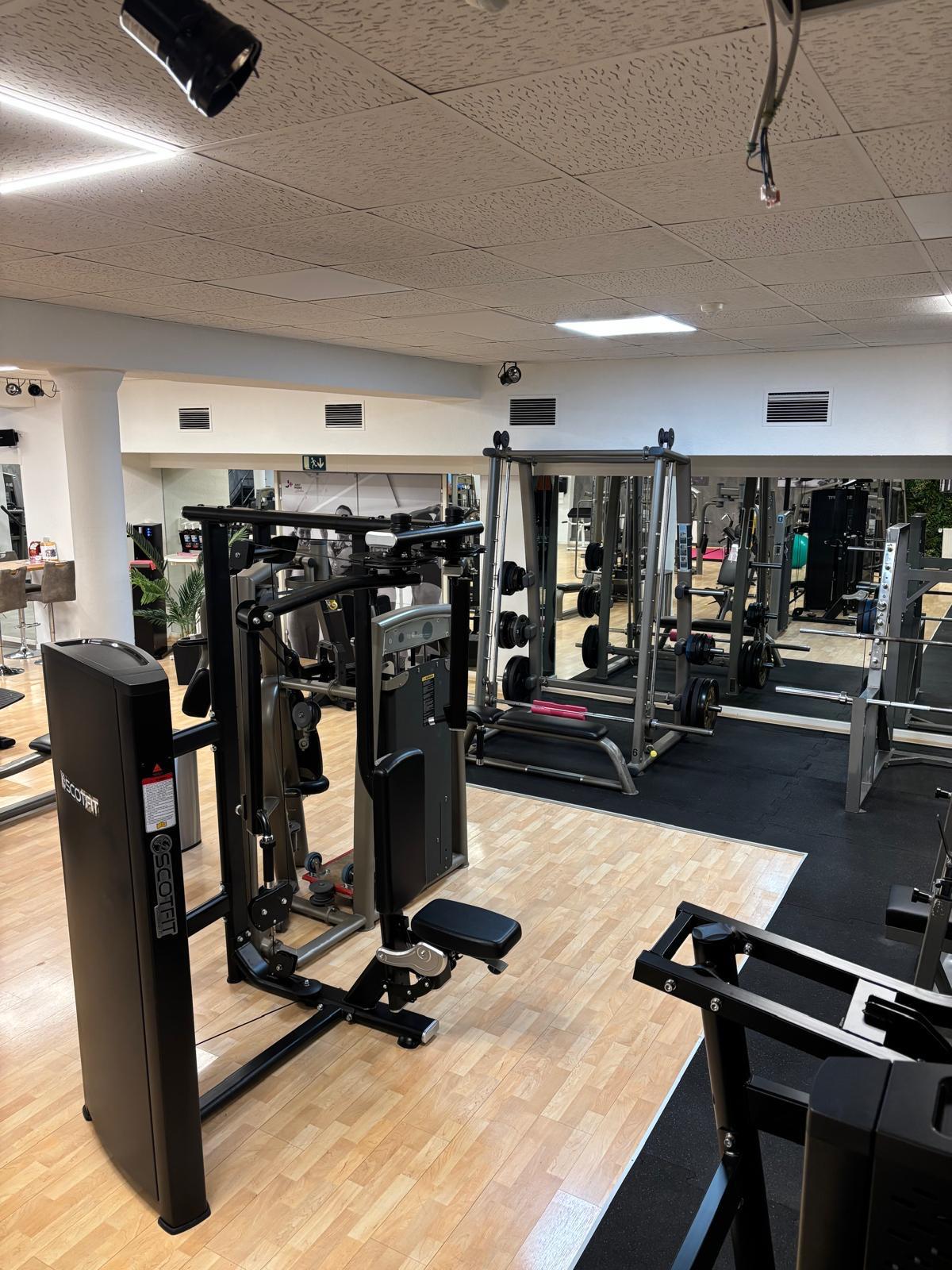 Modern gym with weight machines, free weights, mirrors, and wood and rubber flooring.