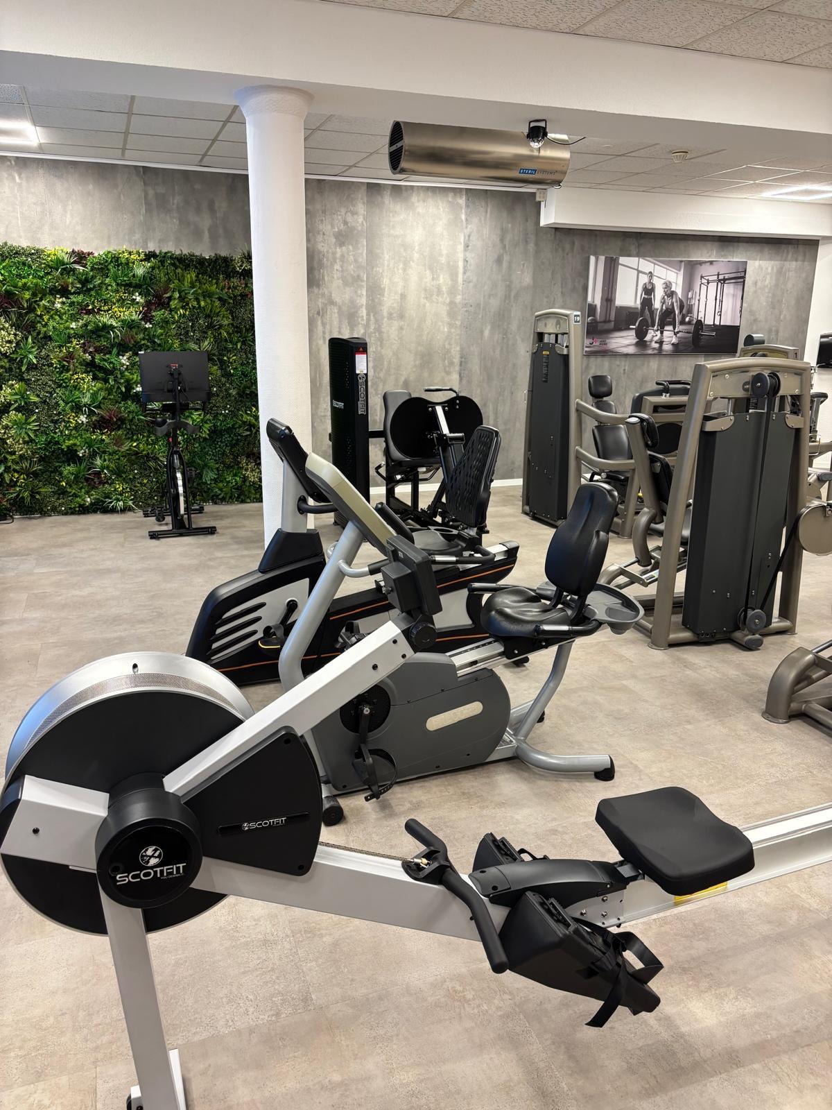 Modern gym interior with rowing machine, stationary bike, weight machines, and vertical garden wall.