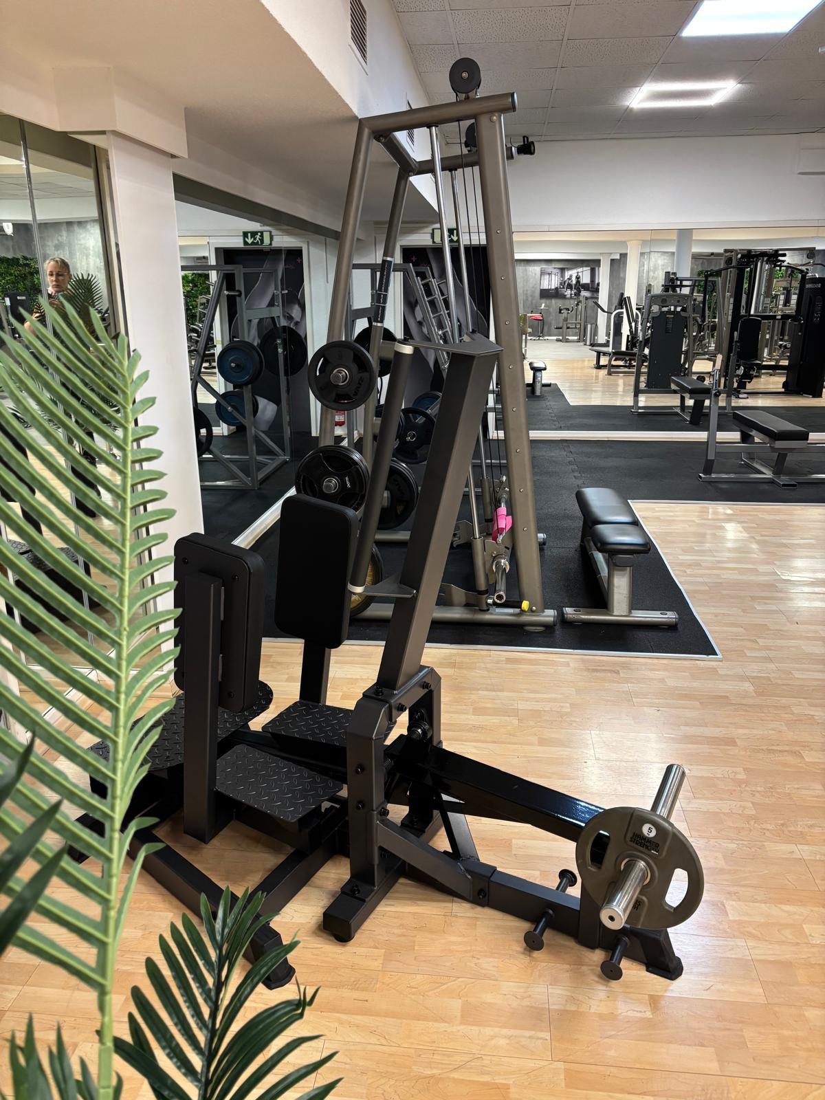 Leg press machine with weights in a gym with mirrors, benches, and wooden floor.