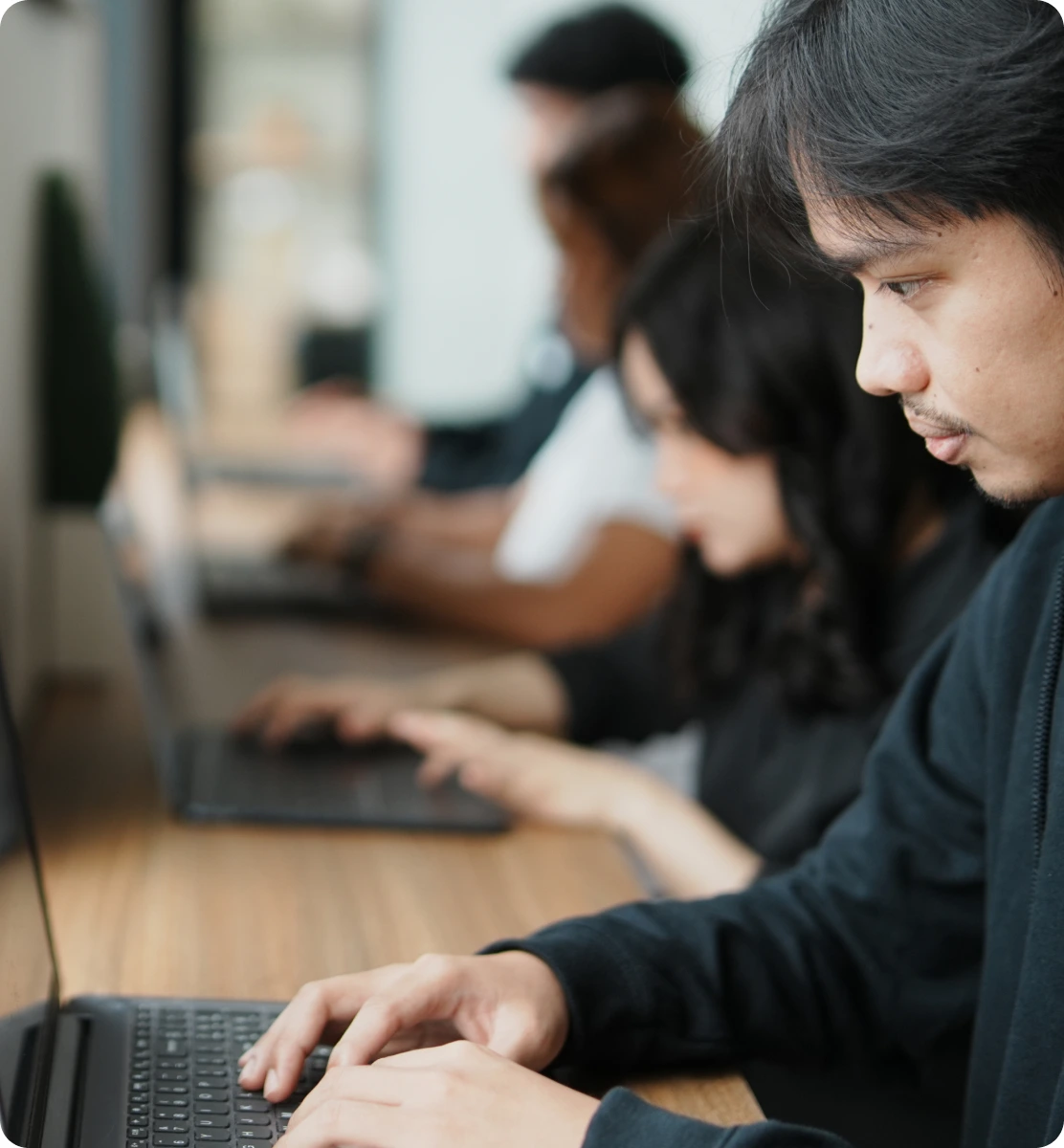     A modern office workspace with employees wearing headphones and working on computers, overlaid with a glowing green digital circuit board graphic. The image represents AI data validation, AI data verification, technology, connectivity, cybersecurity, and focused work in a tech-driven environment.