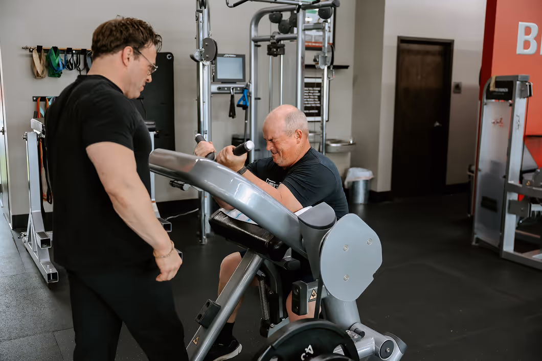 Trainer helping a client with arm curls machine at Todd Smith Fitness