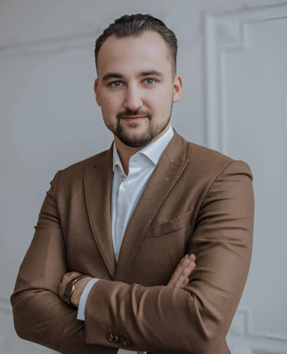 Zygimantas Seskauskis, Business Analyst at Home by NB, wearing a brown jacket and white shirt, looking toward the camera with a calm expression.