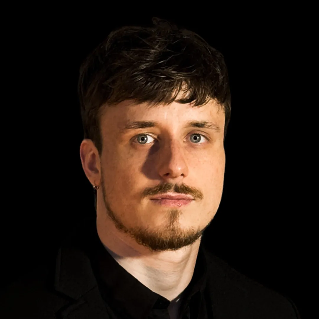 Alex Shkoni, Co-founder and CTO, head-and-shoulders portrait with short dark hair and trimmed beard, wearing a black blazer, facing camera against a dark background.