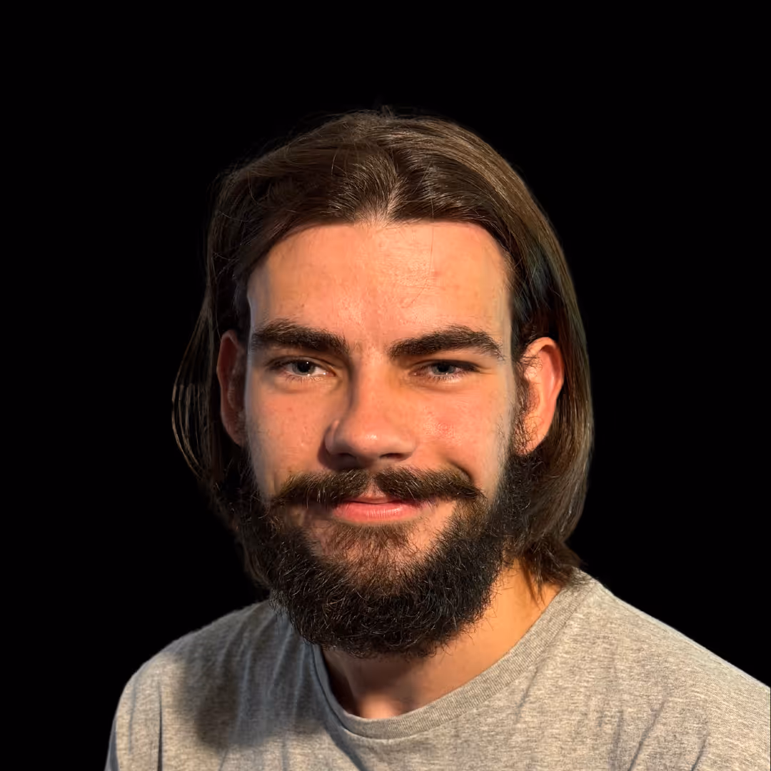 Paul Chepukenas, Customer Success and QA Manager, head-and-shoulders portrait with long brown hair and beard, wearing a light grey shirt, facing camera with a friendly expression against a dark background.