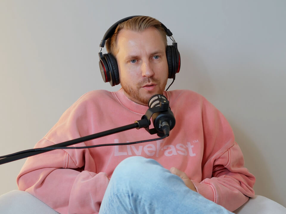Simon mit Kopfhörer und Mikrofon im rosa Hoodie im Podcast-Interview.