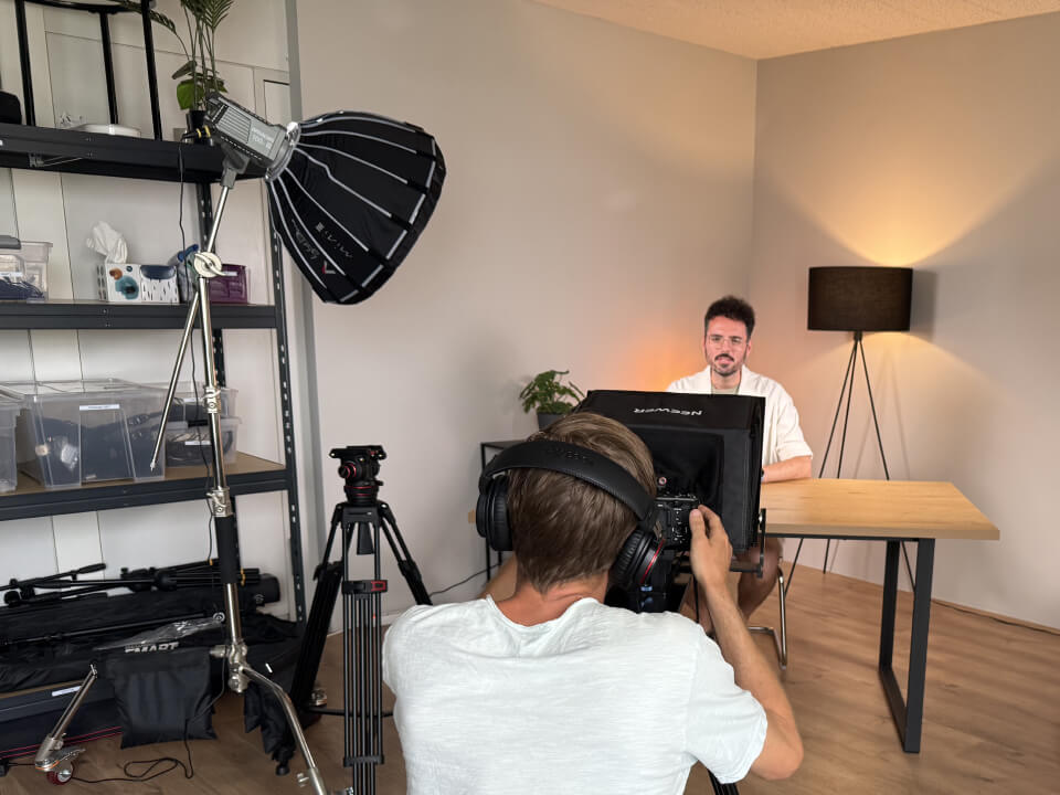 Kamerateam filmt mit Studioleuchten und Stativen in hellem Raum.