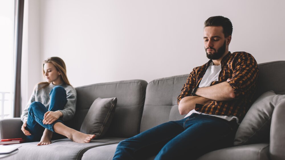 Couple sitting apart and visibly upset, reflecting relationship struggles with different needs.