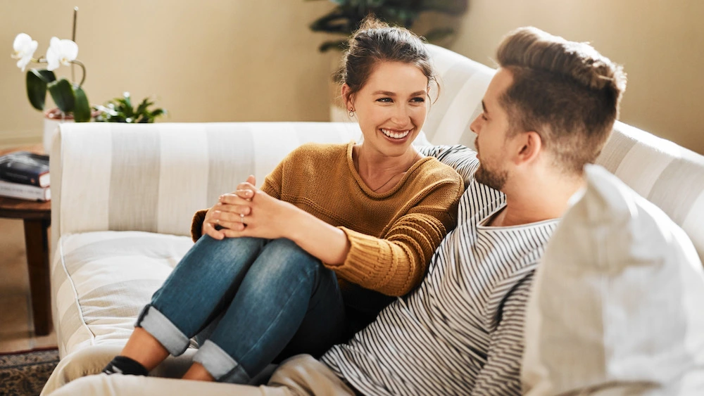 Couple sitting on couch, laughing and looking lovingly, showing open communication.