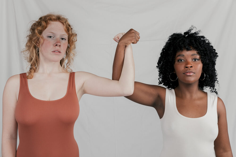 Caucasian and African young women couple making fists.