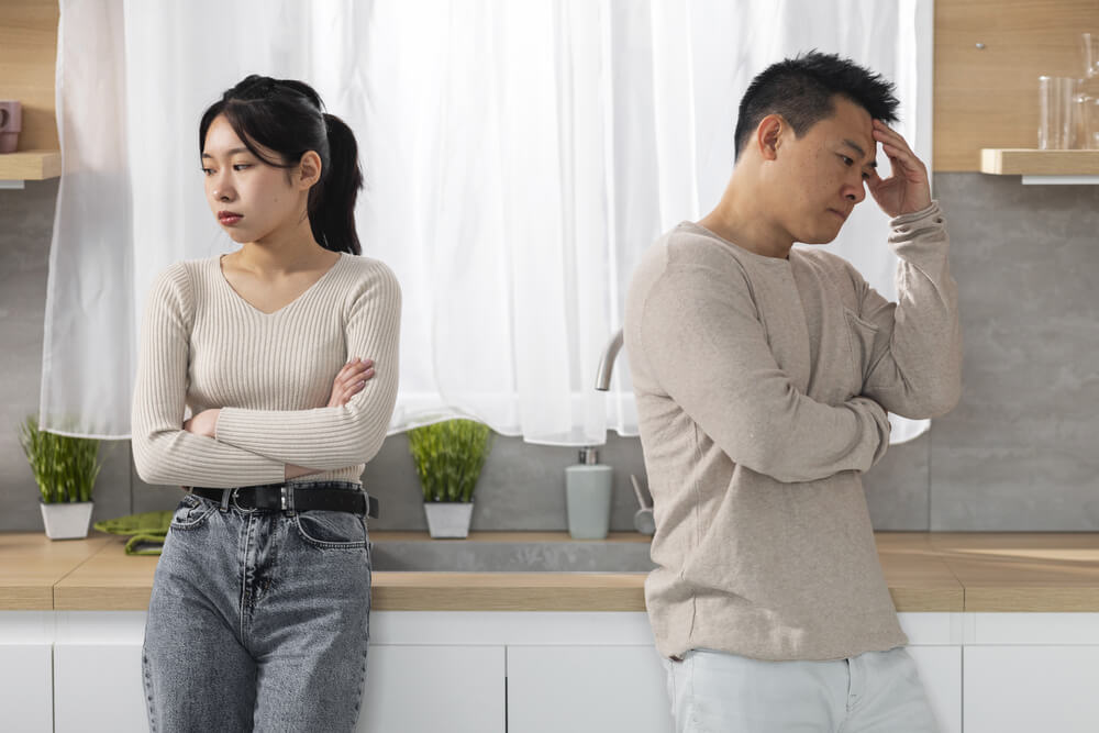 Sad asian couple sit apart, showing tension in their marriage.