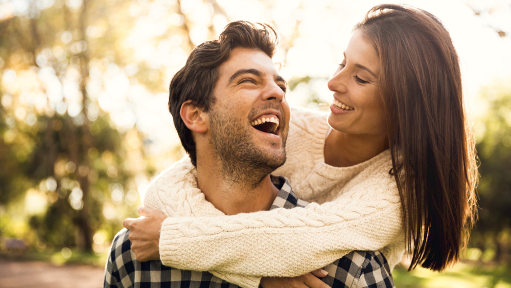 Happy couple piggybacking outdoors in sunny nature, smiling and playful.