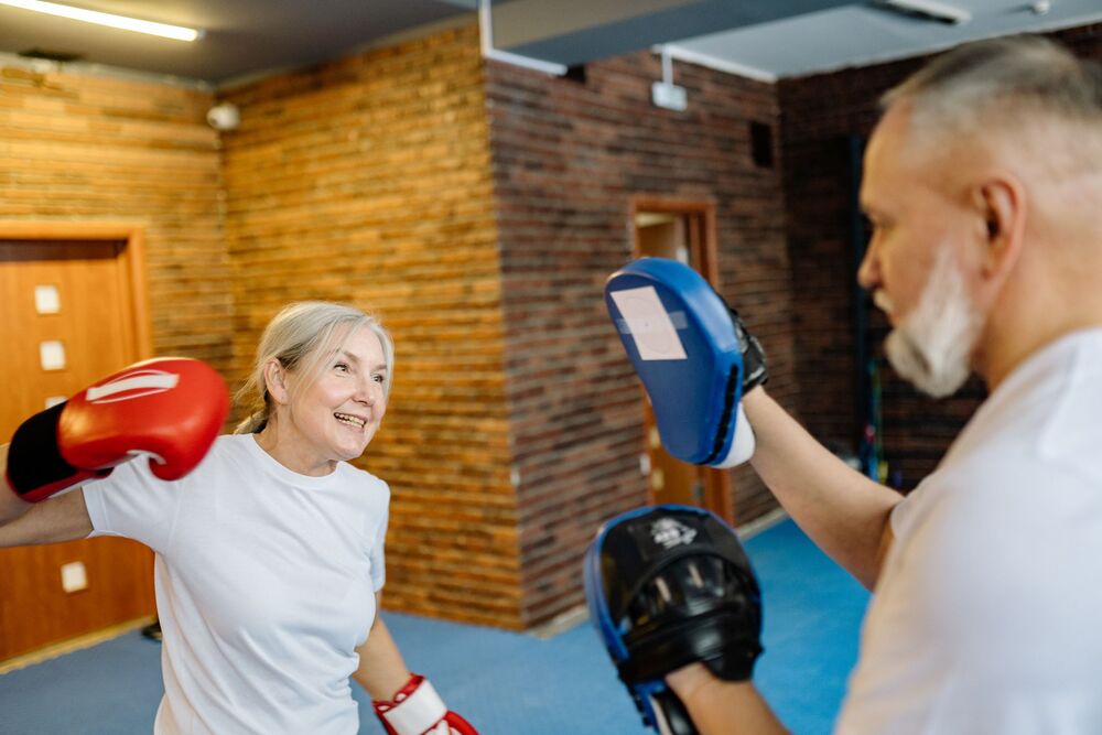 Older couple playfully boxing together indoors, smiling and active.