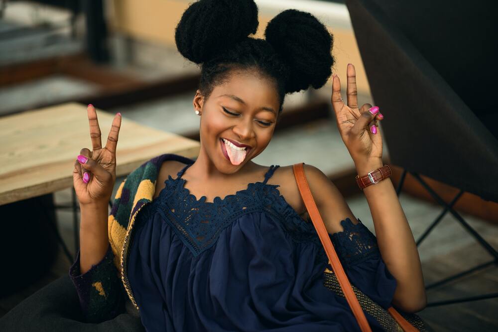 Playful woman smiling with both hands raised in a V sign pose.