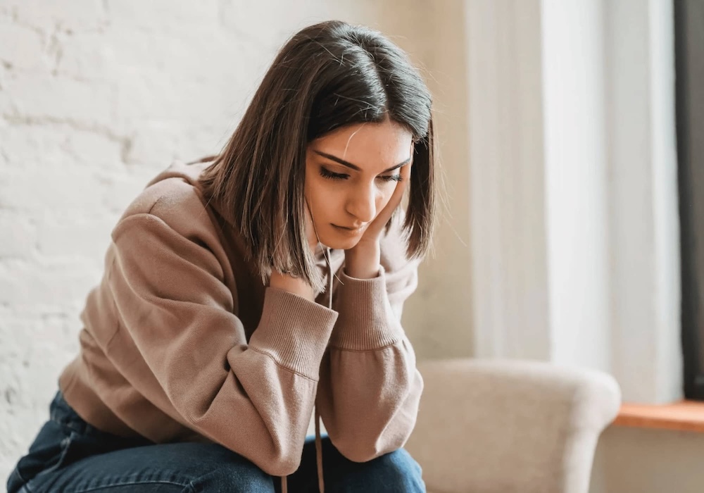 Woman sitting with head in hands, looking worried and stressed.