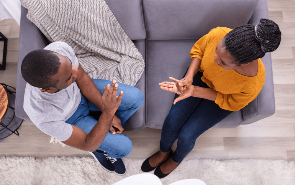 Overhead view of a couple sitting on a couch having a serious discussion, symbolizing open communication and conflict resolution in relationships.