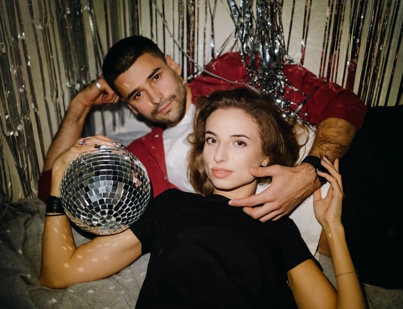 A young couple in cocktail party attire celebrating New Year’s Eve with a disco ball, symbolizing fresh beginnings, joy, and setting practical relationship resolutions together.